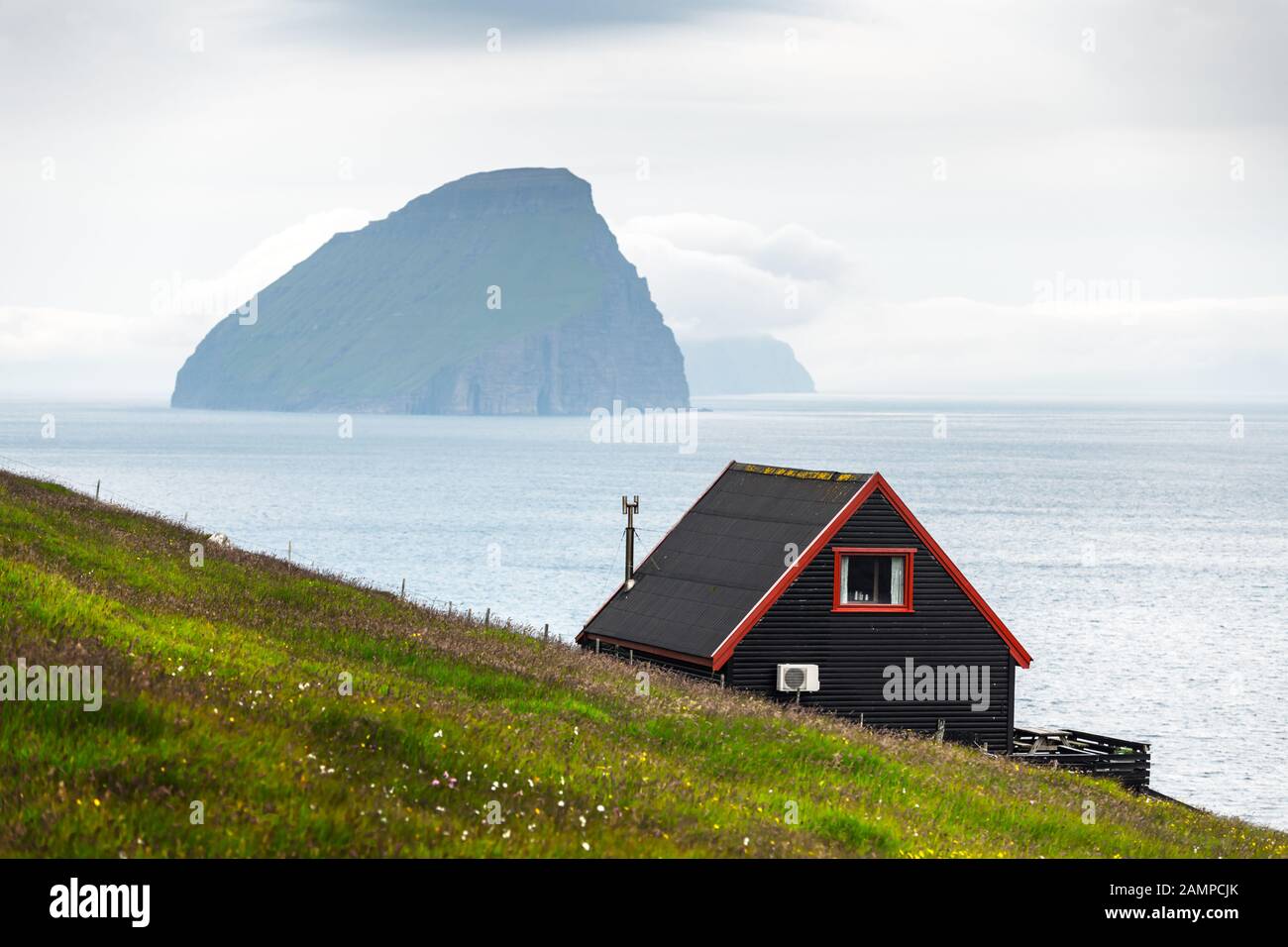 Schwarzes Haus auf dem berühmten färöischen Hexen Finger Trail und der Koltur Insel im Hintergrund. Dorf Sandavagur, Insel Vagar, Inseln der Färöer, Dänemark. Landschaftsfotografie Stockfoto