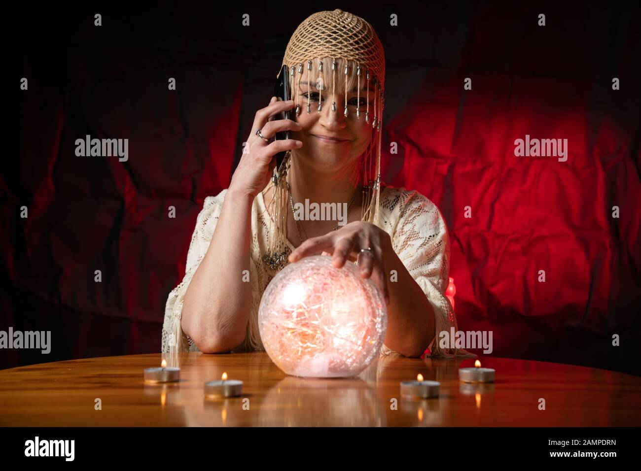 Fortune Teller mit Crystal Ball und Handy auf dem Tisch mit Kerzen. Smartphone-, Online- oder Anrufkonzept Stockfoto