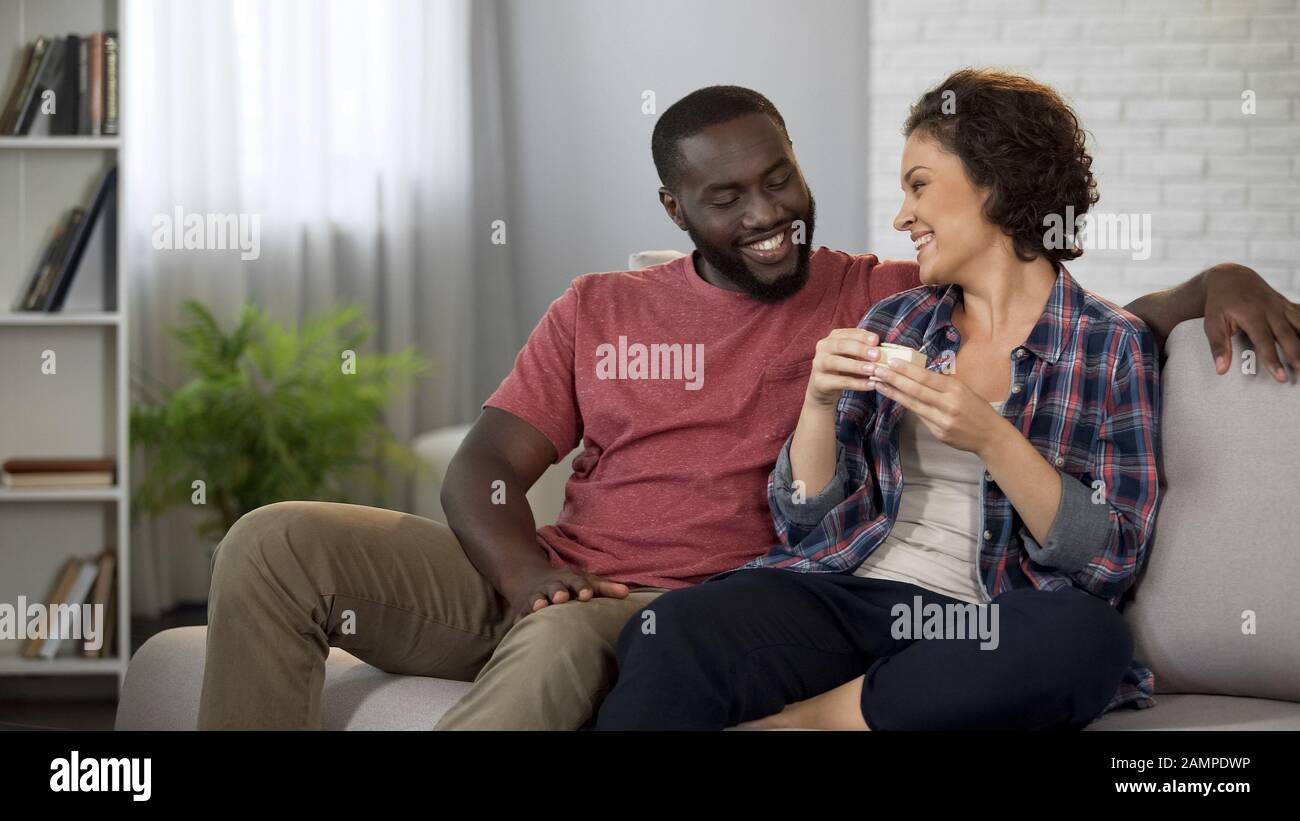 Glücklicher afroamerikanischer Mann, der seine glückliche Freundin mit Geschenk öffnet Stockfoto