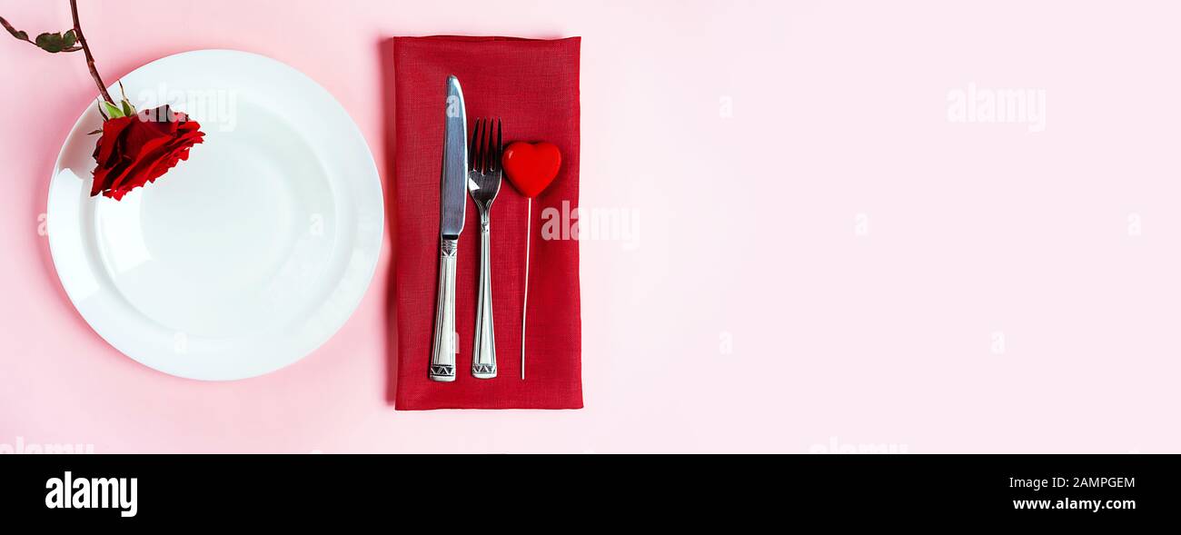 Romantisch gedeckten Tisch für Valentines Tag oder Abendessen Datum Feier Hochzeit. Valentines Tag Konzept mit rote Rose Bud White Platten auf Pastell rosa Tischdecke Hintergrund. Flach, Ansicht von oben kopieren. Stockfoto