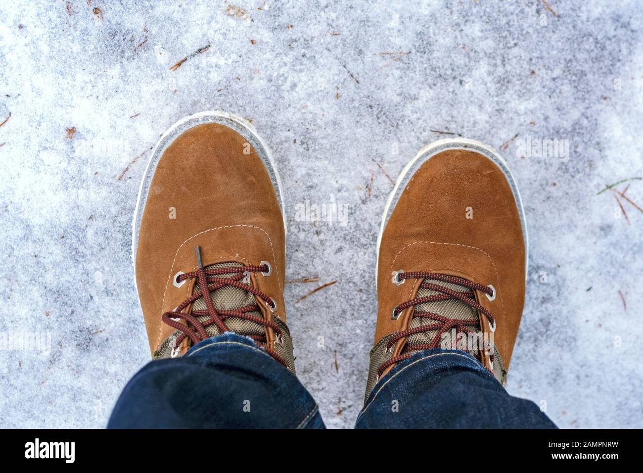 Zwei rote Stiefel auf den Füßen eines Mannes, der auf der eisigen Oberfläche des Sees steht. Stockfoto