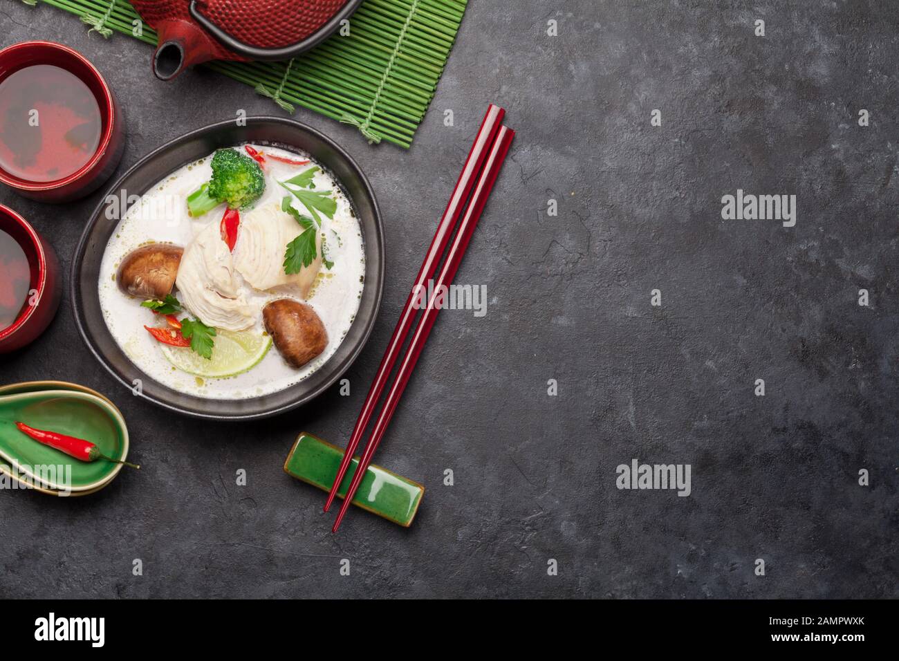 Tom Kha traditionelle thailändische Suppe mit Huhn, Pilzen, Kokosmilch und heißen Gewürzen. Mit grünem Tee in Topf und Schüsseln. Draufsicht mit Kopierbereich Stockfoto