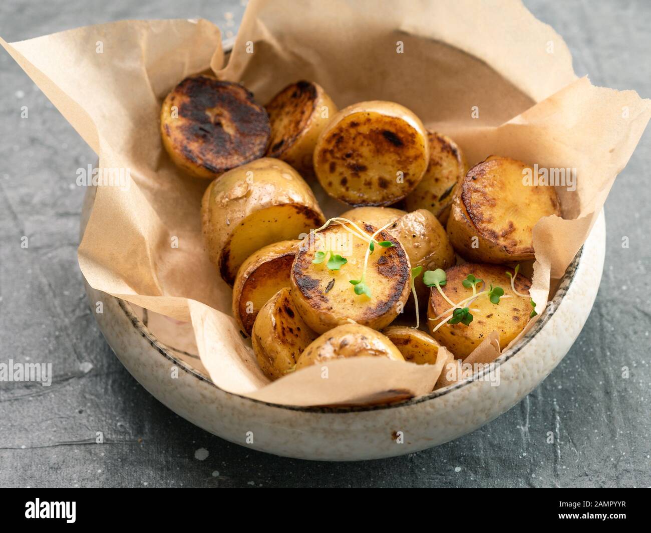 Gebratene baby Kartoffeln und microgreen in Handwerk Platte auf grauem Hintergrund. Baby Kartoffel Hälfte, geröstet. Stockfoto