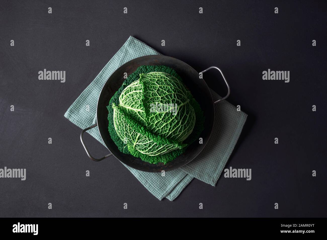 Grünkohl in einer rostigen eisernen Pfanne auf einem Küchentuch auf schwarzem Grund. Gesunde Ernährung. Ernährung. Overhead von savoyenkohl. Frisches Gemüse. Stockfoto