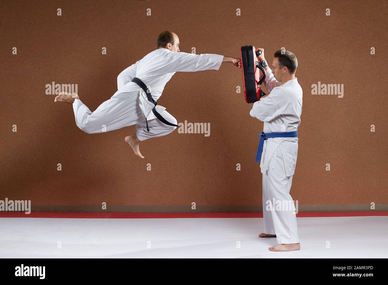 Mit einem schwarzen Gürtel, ein Athlet beats blow Hand in einem Sprung auf dem Simulator Stockfoto