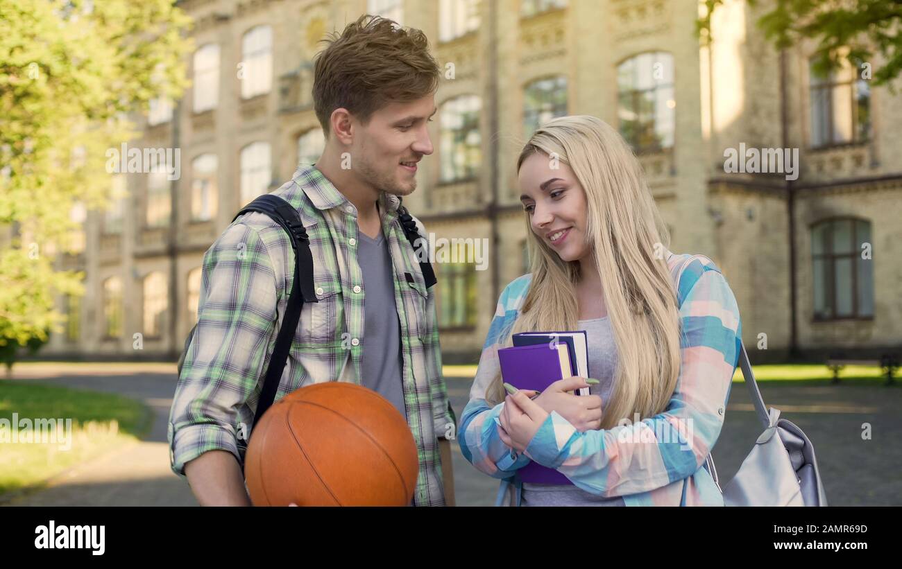 Student hält Ball, flirtet mit hübschem Mädchen in der Nähe der Universität und bittet um Datum Stockfoto