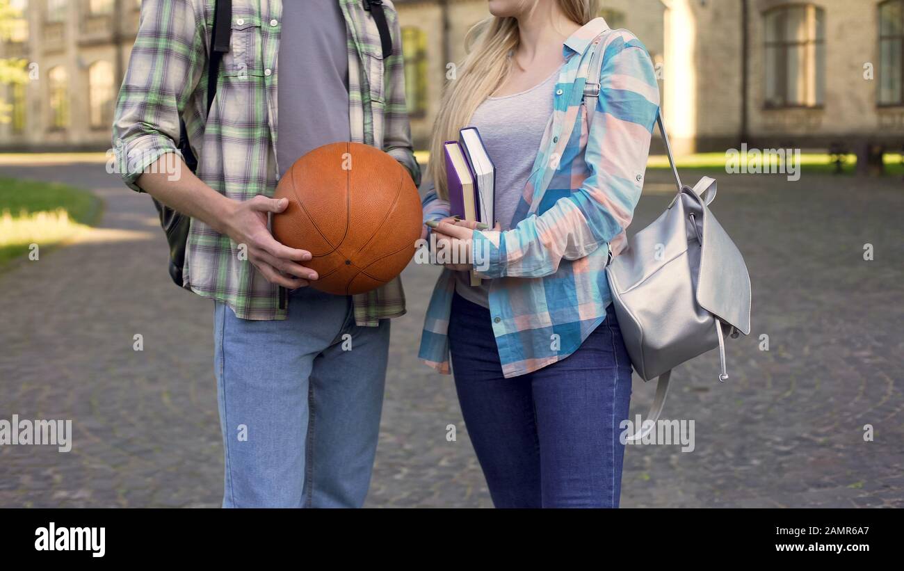Studenten-Mädchen, die Bücher halten und mit Sportlern in der Nähe des College plaudern, flirten Stockfoto
