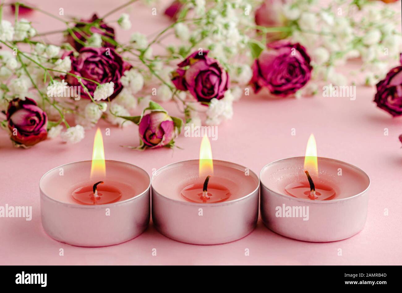 Aromatherapie-Konzept. Drei brennende Kerzen und trockene Rosen auf rosa Hintergrund. Stockfoto