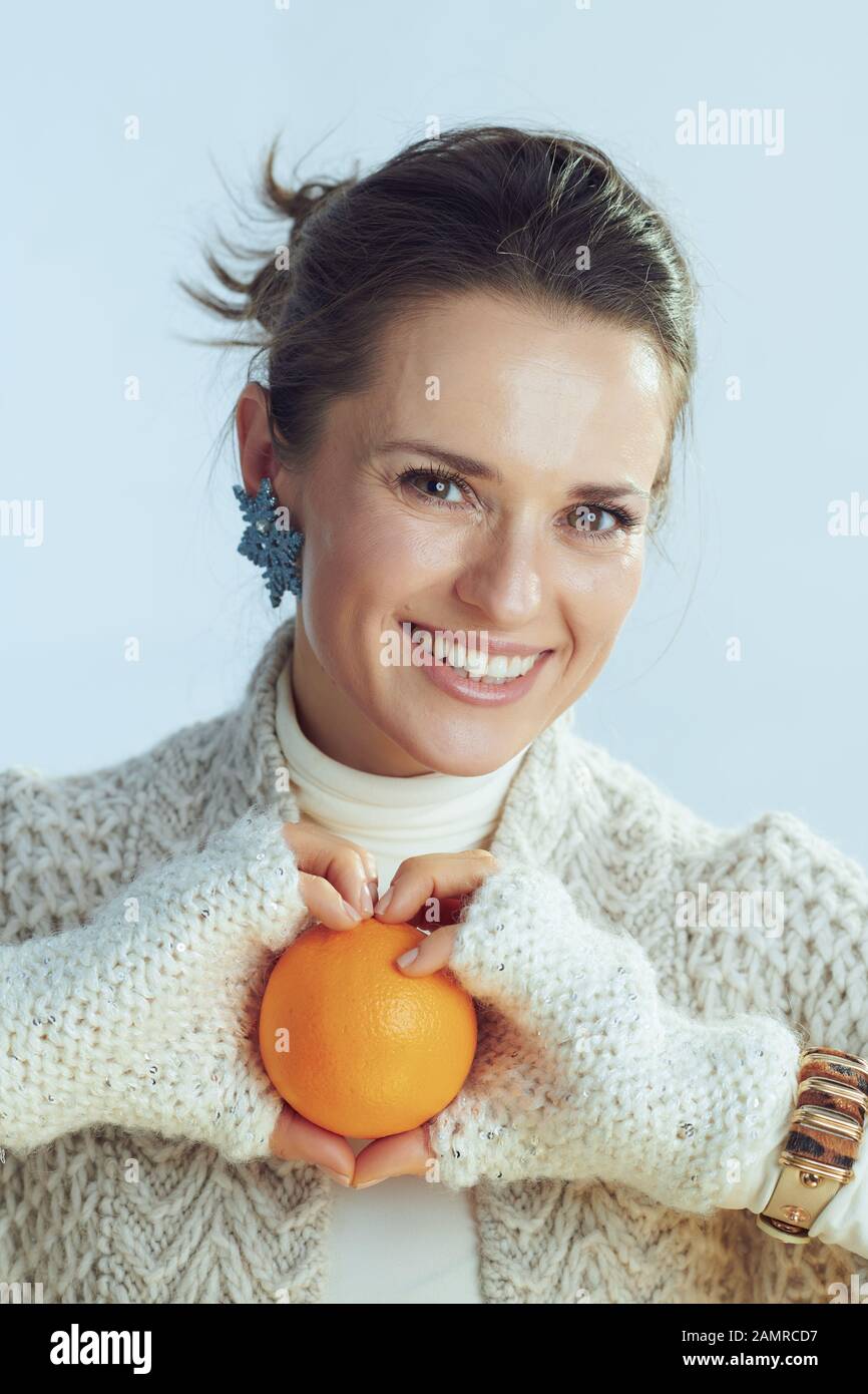 Porträt von fröhlicher, stilvoller Frau mit Rollkragen-Pullover und Strickjacke, orange isoliert auf hellblauem Hintergrund. Stockfoto