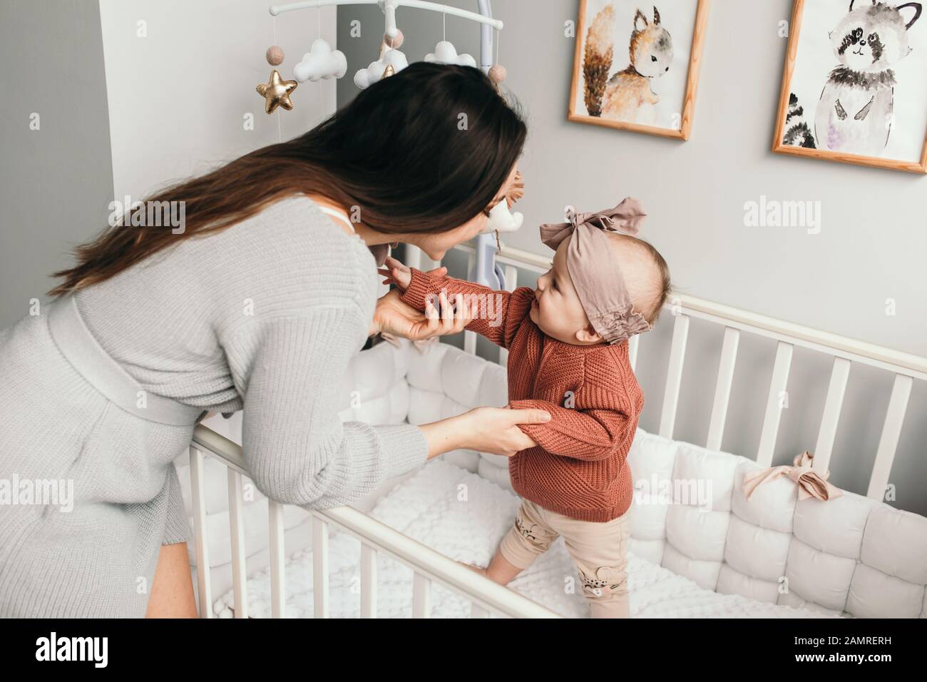 Schönes kleines Mädchen im Bett mit ihrer Mutter, helle, stilvolle Einrichtung. Versuch zu stehen. Begriff der Brüderlichkeit. Stockfoto