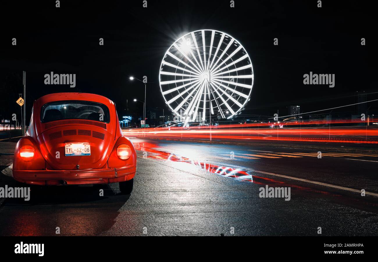 Angelopolis, Puebla de Zaragoza, Mexiko, 15. Oktober 2018 - Straßenfoto des alten Autos Volkswagen Beetle mit Riesenrad der Puebla-Stadt in der Nacht. Lange Exposition der mexikanischen Straße. Stockfoto