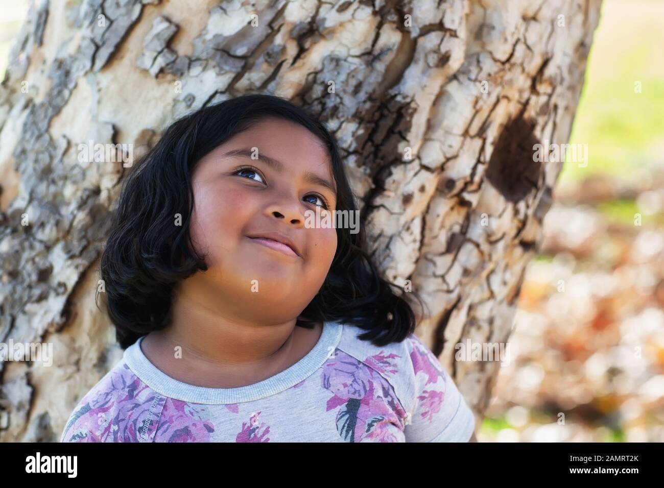 Ein 9 Jahre altes Mädchen träumt, während es sich an einen Baumstamm lehnt. Stockfoto