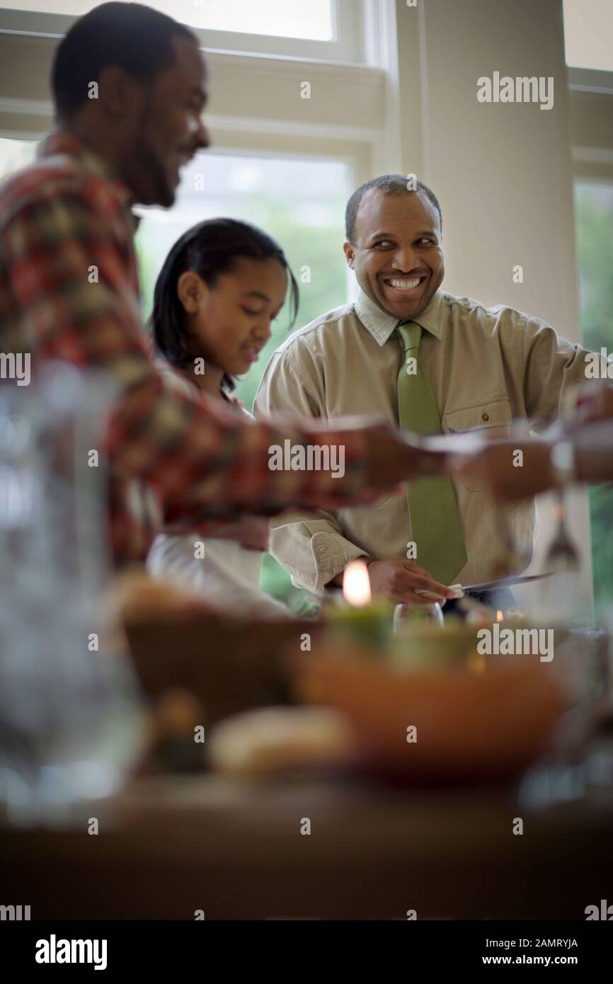 Ein mittelerwachsener Mann lächelt, während er sich mit seiner Familie zum Abendessen bedient. Stockfoto