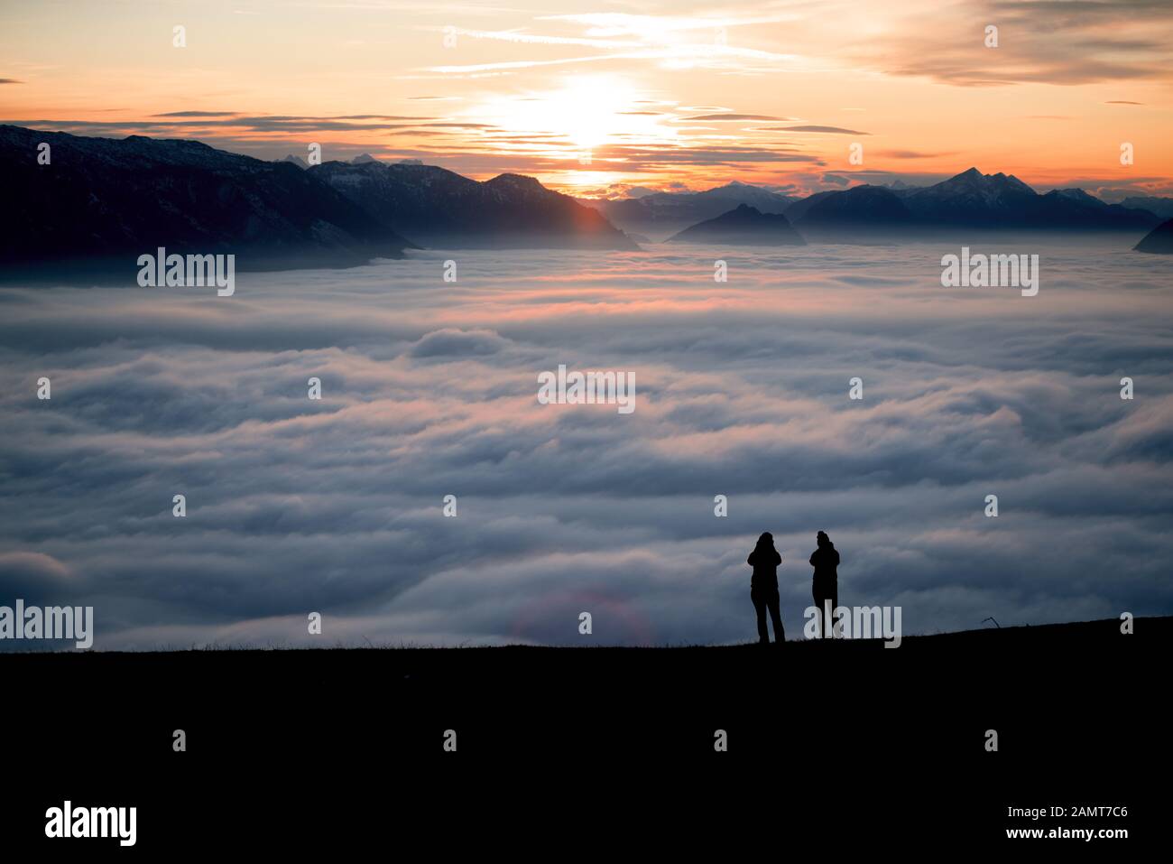 Silhouette zweier Frauen auf einem Berggipfel bei Sonnenuntergang mit Blick auf die Aussicht, Salzburg, Österreich Stockfoto