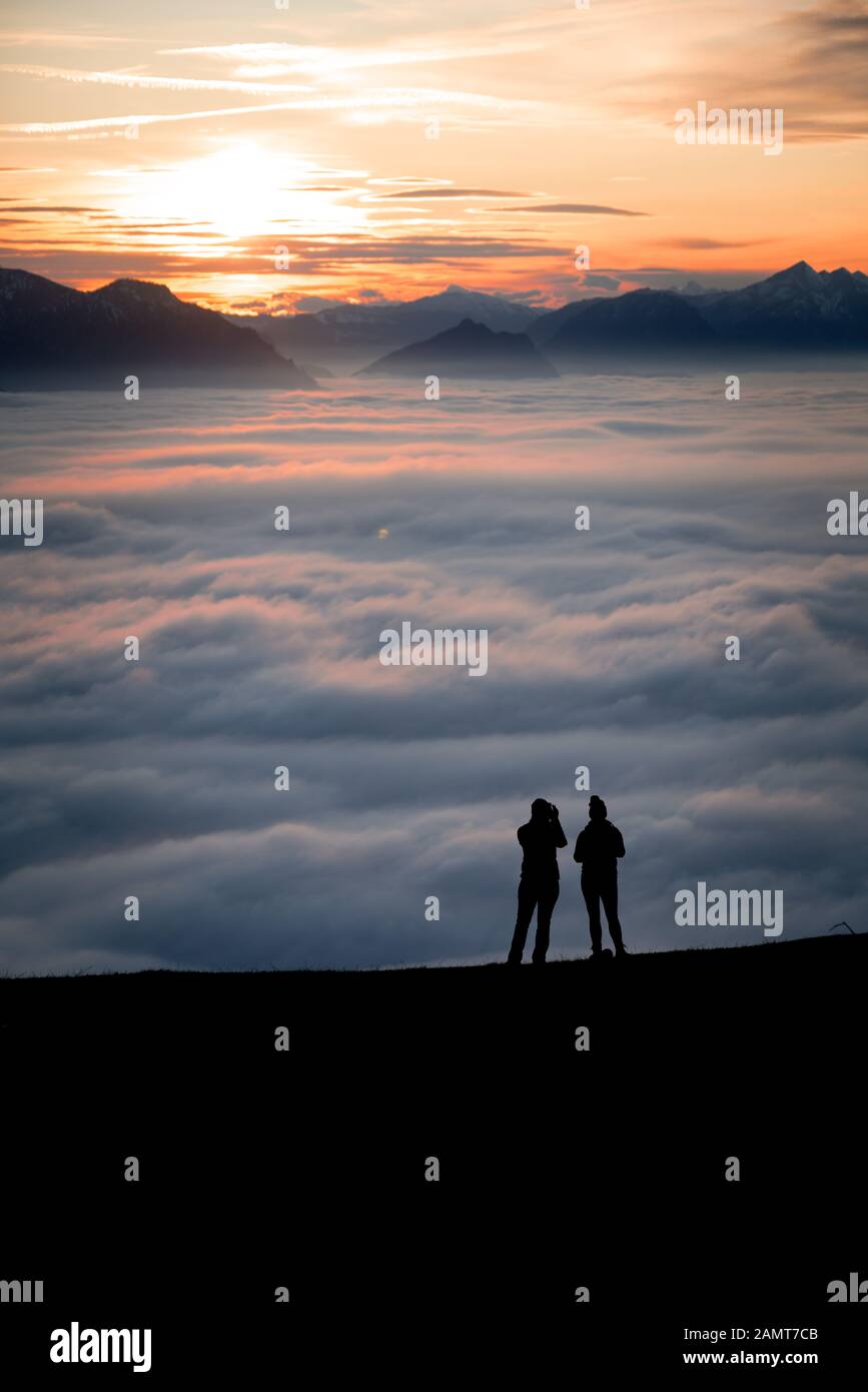 Silhouette zweier Frauen auf einem Berggipfel bei Sonnenuntergang mit Blick auf die Aussicht, Salzburg, Österreich Stockfoto