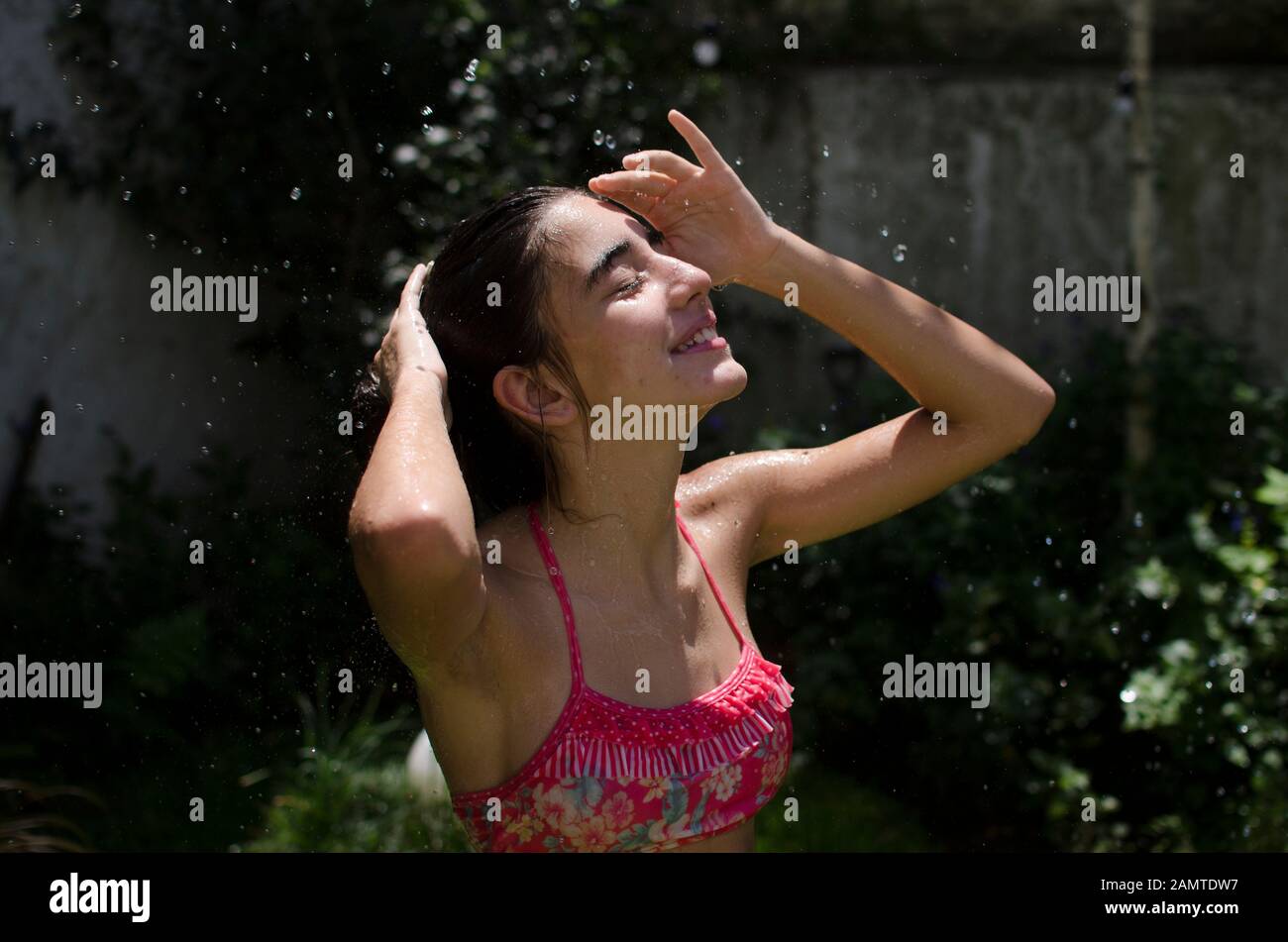 Teenager-Mädchen, das in einem Garten steht, der sich unter einem Wassersprinkler abkühlt, Argentinien Stockfoto