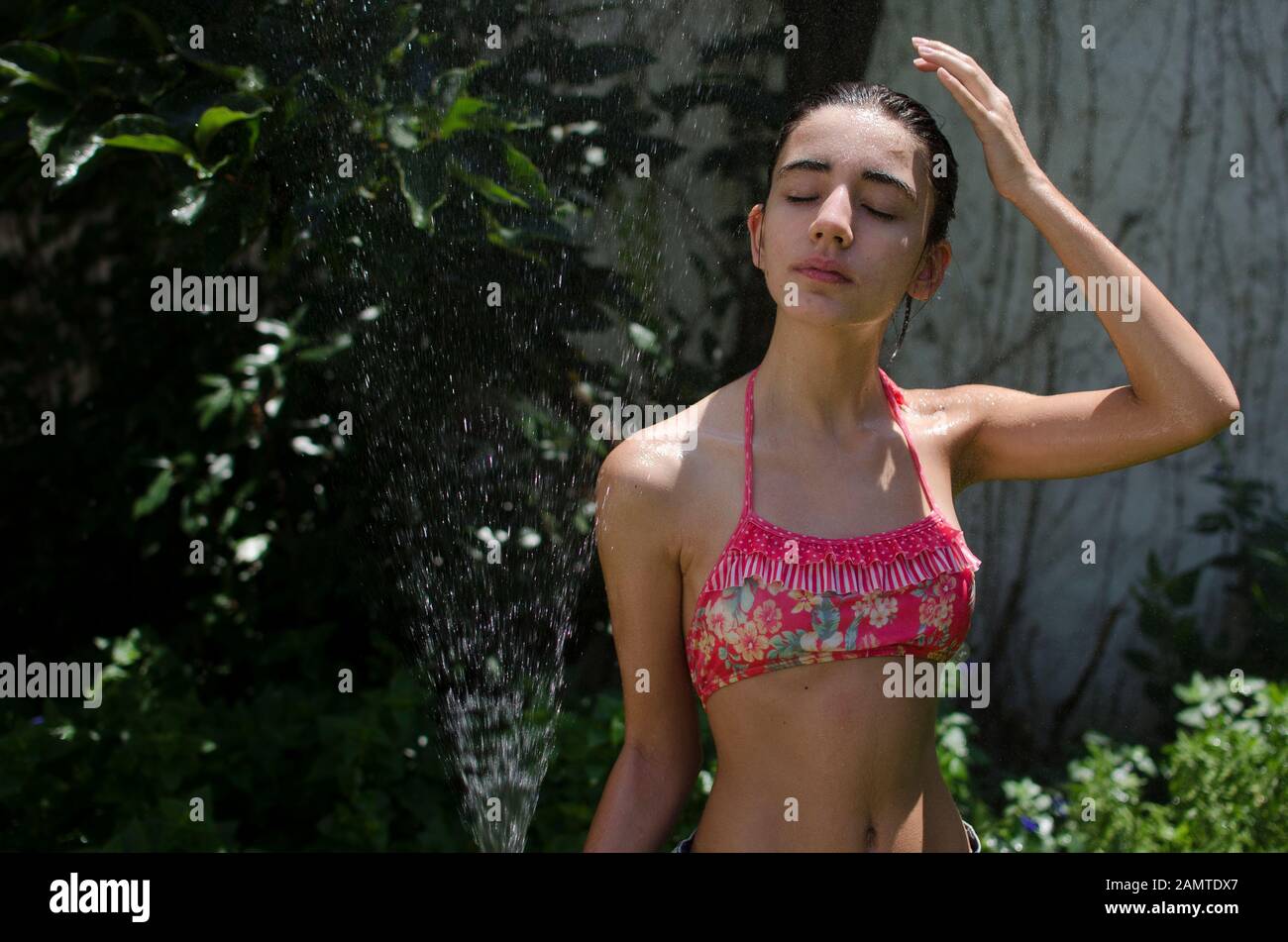 Teenager-Mädchen, das in einem Garten steht und sich mit einem Wasserschlauch abkühlt, Argentinien Stockfoto
