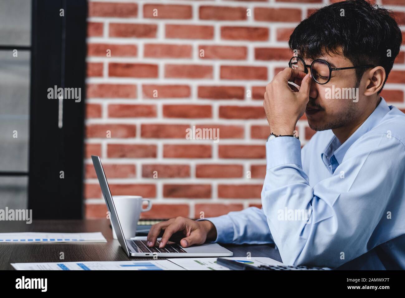 Asiatische Geschäftsmann Stress und Kopfschmerzen beim Arbeiten mit Laptop auf dem Schreibtisch bei der moderne Büro. Business fail Konzept. Mann gefangen Auge wenn überarbeitet. Stockfoto
