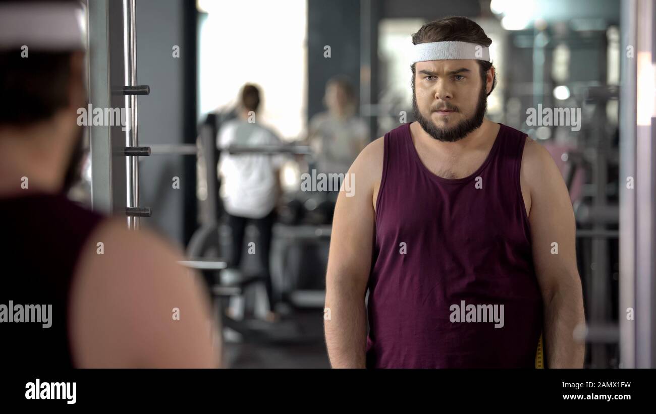 Fetter Mann mit Blick auf Spiegelreflexionen im Fitnessstudio, mentales Training vor dem Training Stockfoto