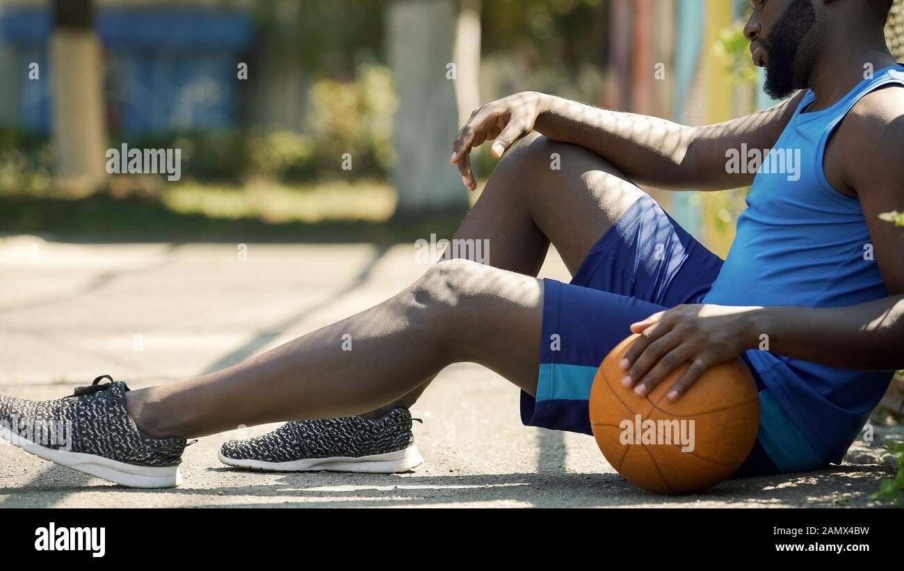 Ärgern Sie den afroamerikanischen Basketballspieler, der auf dem Boden sitzt und den Ball hält Stockfoto