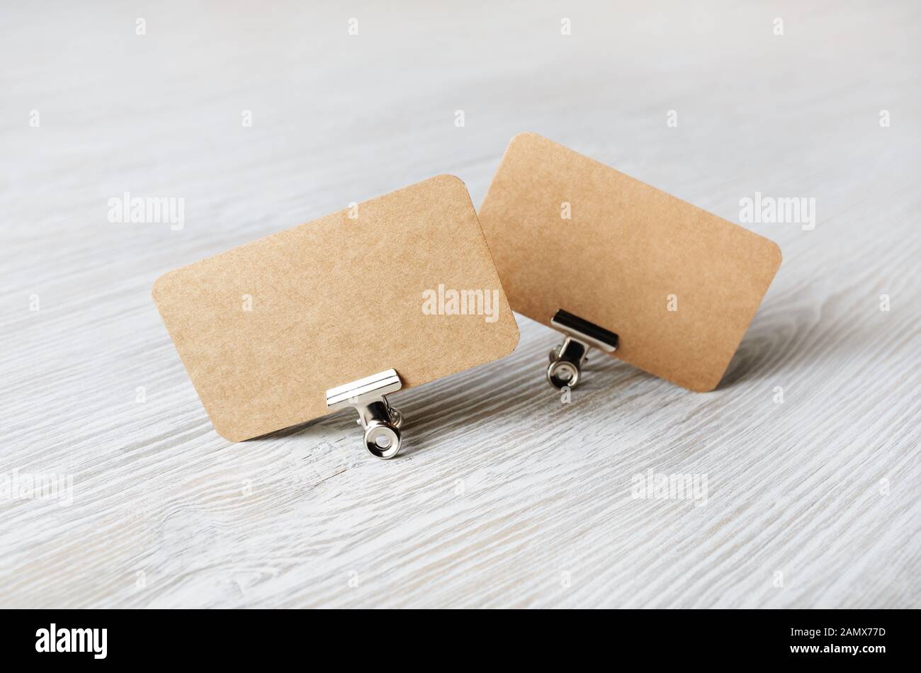 Zwei leere Kraftpapier Visitenkarten und Metall binder clips auf hellem Holz Tisch Hintergrund. Stockfoto