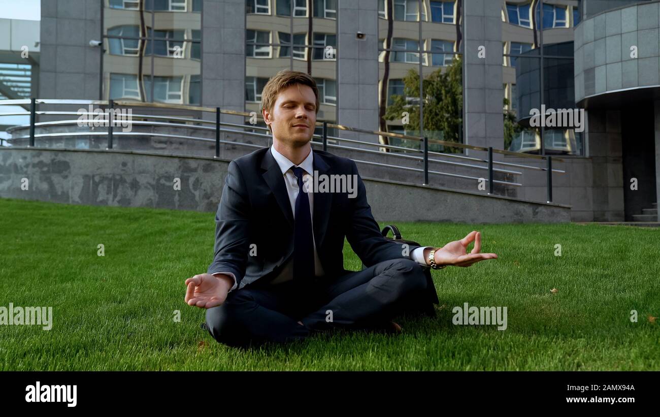 Junger Bürochef sitzt in lotus-position und meditiert auf Gras, Freiheit Stockfoto