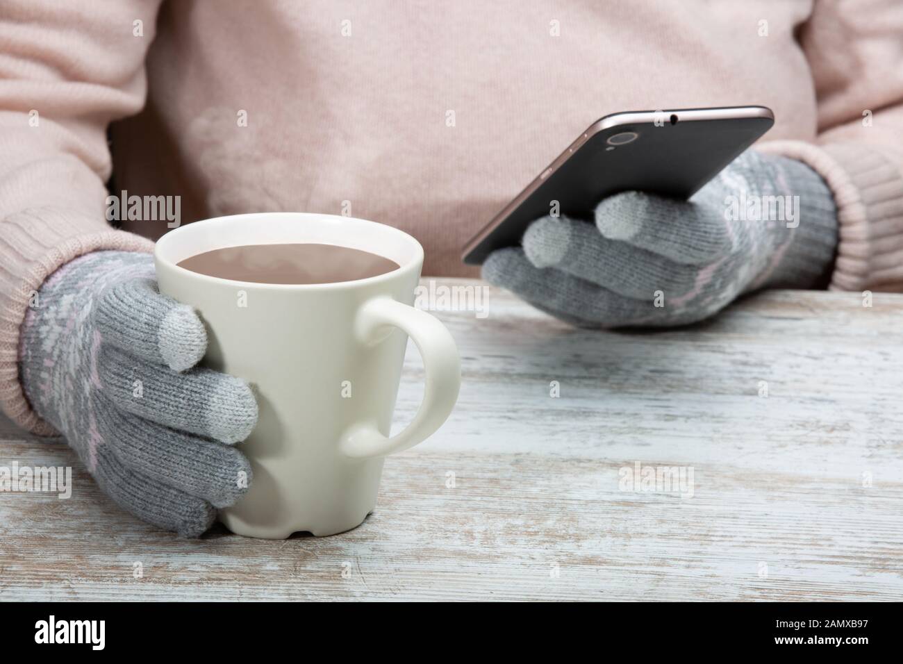 Ein Mann in warme Kleidung sitzt mit einer Tasse heißen Getränk in einem Straßencafe. Rest im Winter Sport. Eine Frau hält ein Handy in der Hand. Close-up Stockfoto