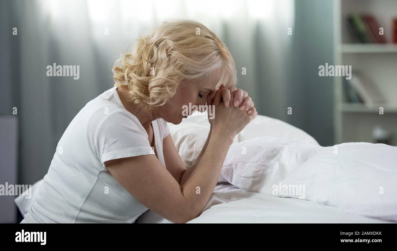 Frau im mittleren Alter betet, sitzt auf dem Boden neben Bett, Glaube und Hoffnung, Religion Stockfoto