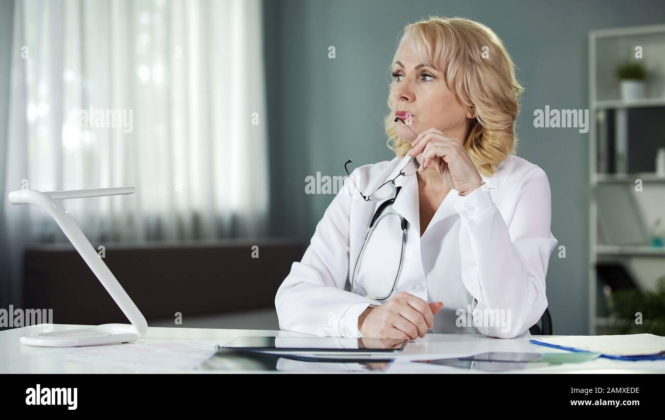 Nachdenklicher weiblicher Arzt, der am Tisch sitzt, die Patientenergebnisse analysiert, die Diagnose Stockfoto