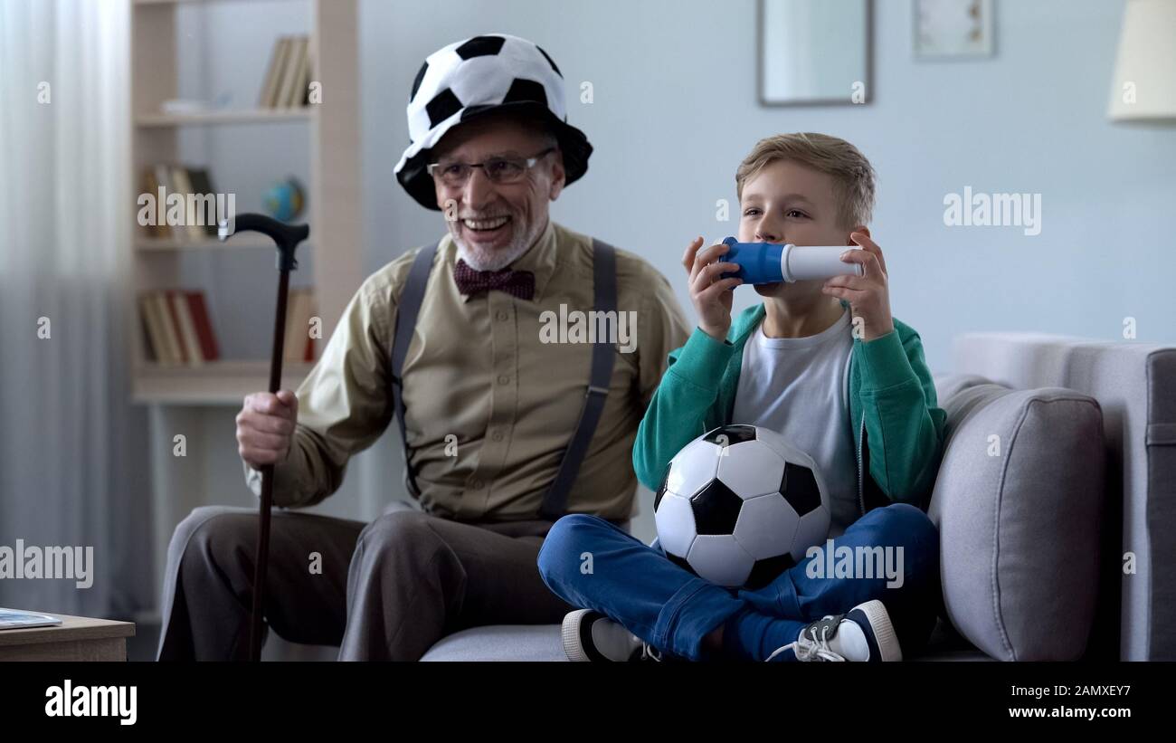 Opa in verrückter Fußballmütze und Junge jubeln für Nationalmannschaft mit Fanhorn Stockfoto