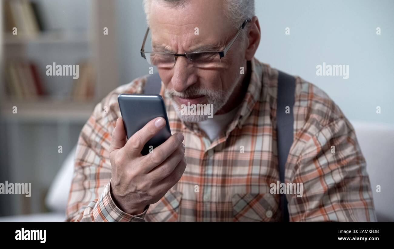 Der alte Mann schaut ungläubig auf Handy, neue Technik für ältere Menschen kompliziert Stockfoto