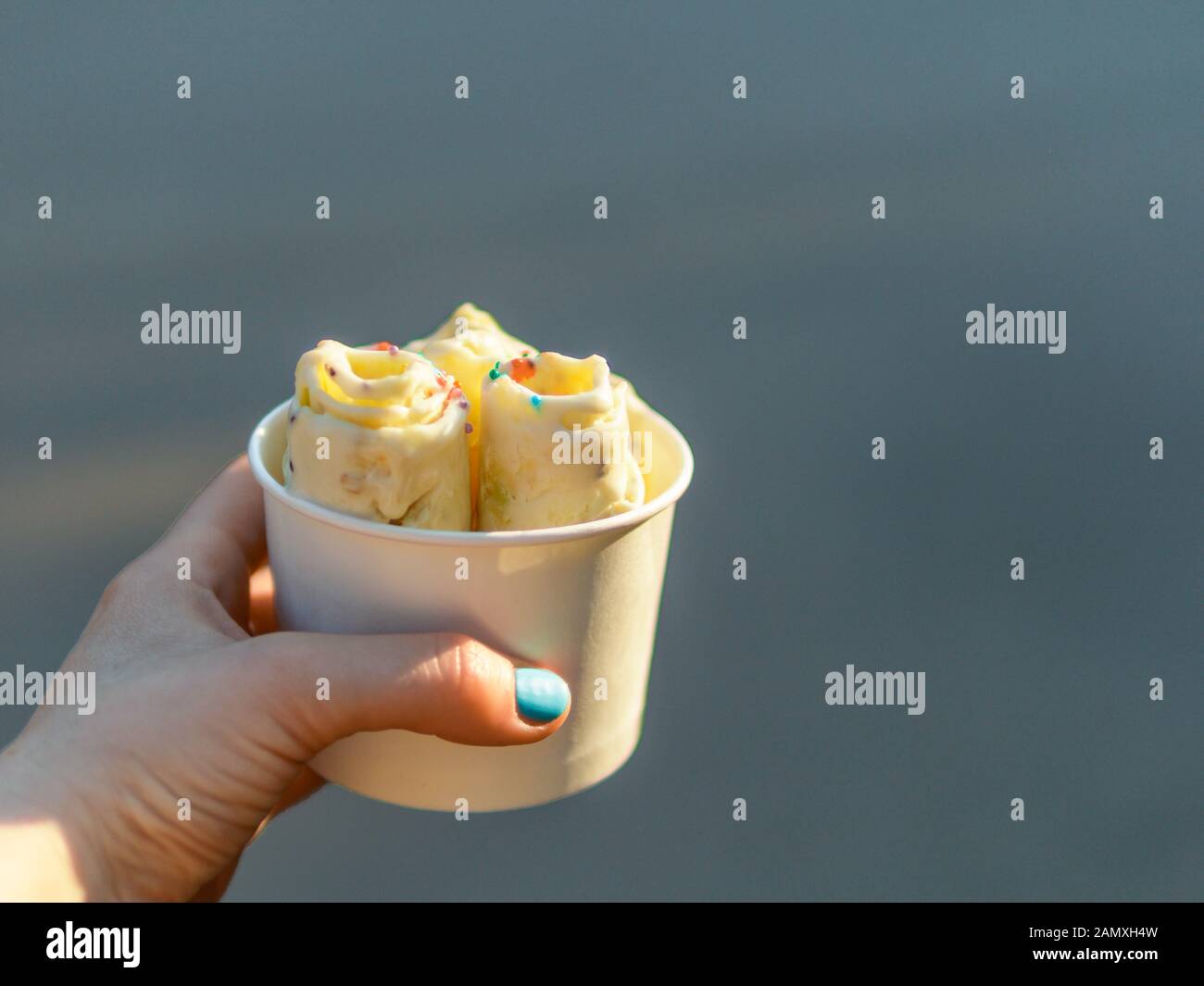 Eiscreme in der Konusschale in der Hand der Frau gerollt. Frau hält Konusbecher mit kiwi-bananen-Eiscreme im thailändischen Stil. Im Freien. Natürliches hartes Tageslicht. Platz nach rechts kopieren. Stockfoto