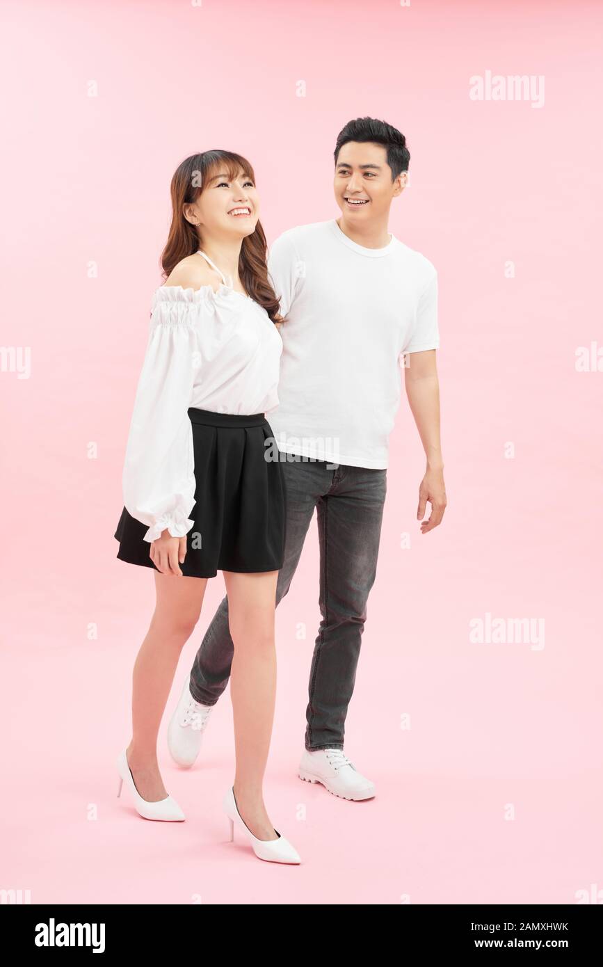 Langes Porträt des glücklichen Paares im lässigen Outfit, das auf pinkfarbenem Hintergrund vorwärts geht Stockfoto