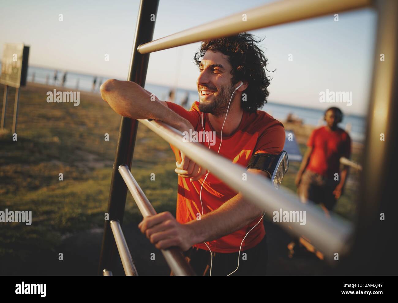 Porträt eines lächelnden jungen athletischen Mann genießen die Musik von seine Kopfhörer Ausruhen nach Training im Fitnessbereich im Freien Stockfoto