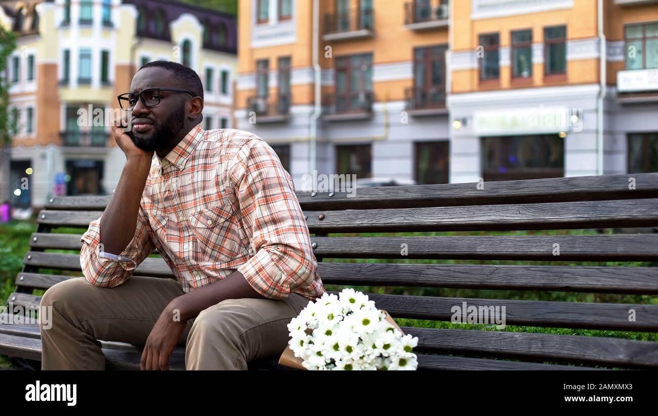 Blinder Termin, nervöse junge Mann wartet auf Mädchen, sitzende Parkbank mit Blumen Stockfoto