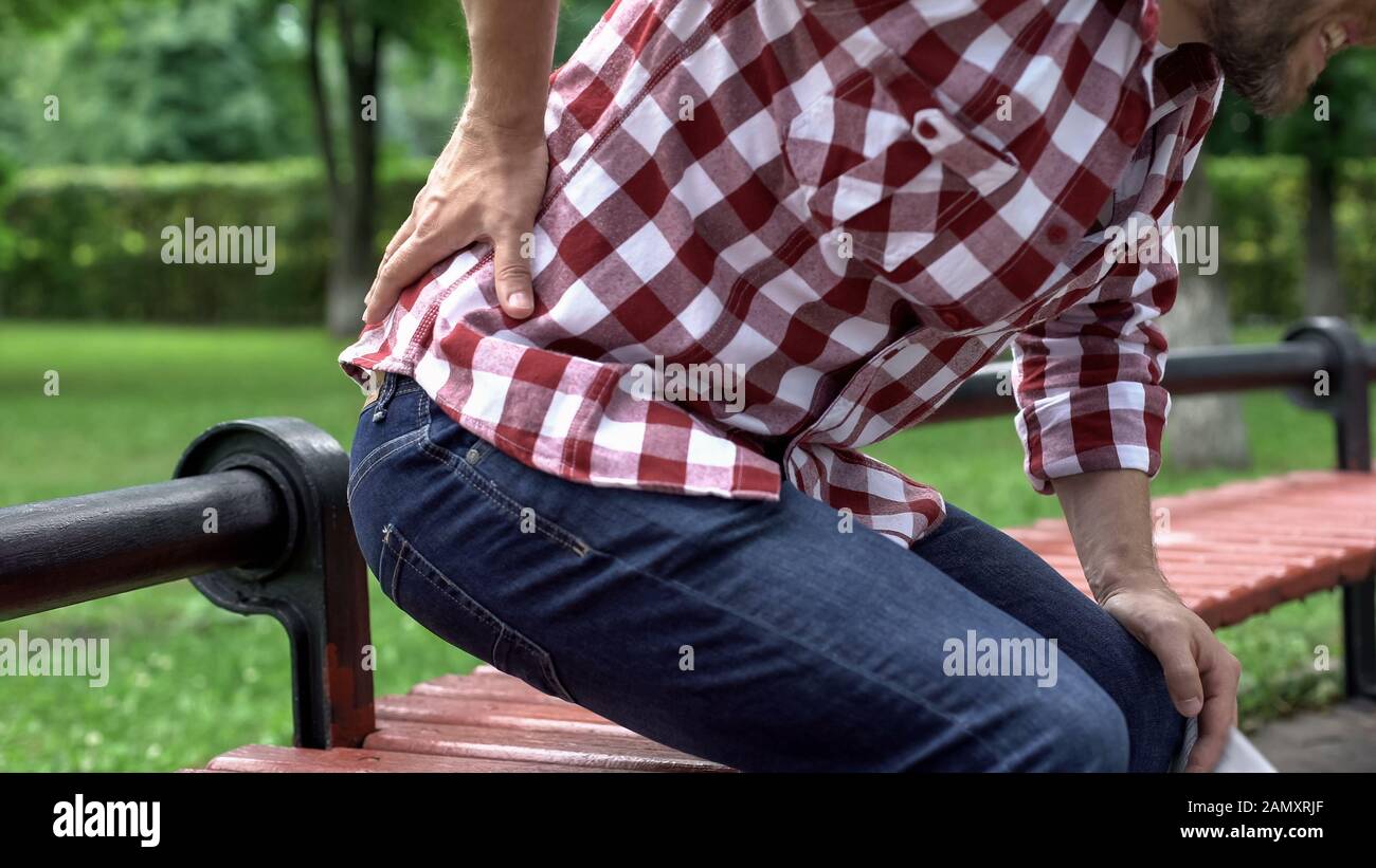 Der Mann leidet unter Schmerzen im unteren Rücken, liest die Zeitung im Park, verdichtete Nervenwurzeln Stockfoto