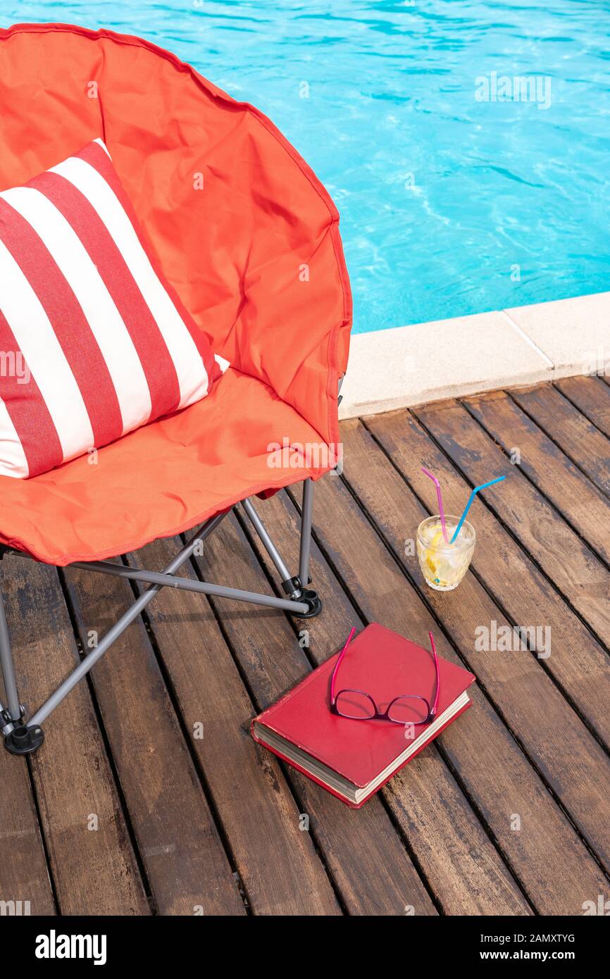 Sommerszene mit Schwimmbad, Stuhl, Getränk und Buch. Konzept für Urlaub oder Freizeit im Sommer. Kopierbereich Stockfoto