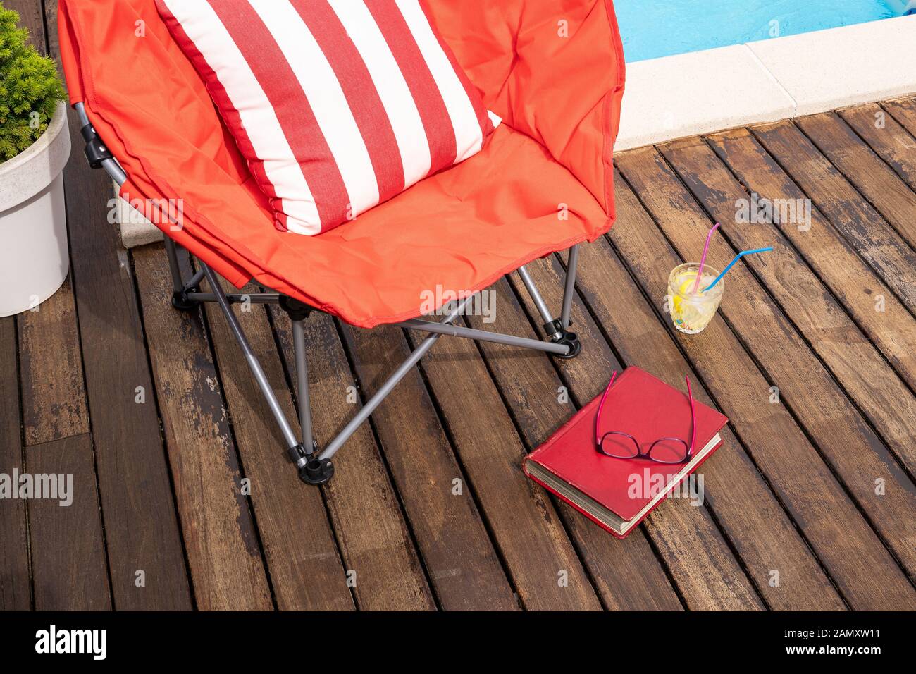 Sommerszene mit Schwimmbad, Stuhl, Getränk und Buch. Konzept für Urlaub oder Freizeit im Sommer. Kopierbereich Stockfoto