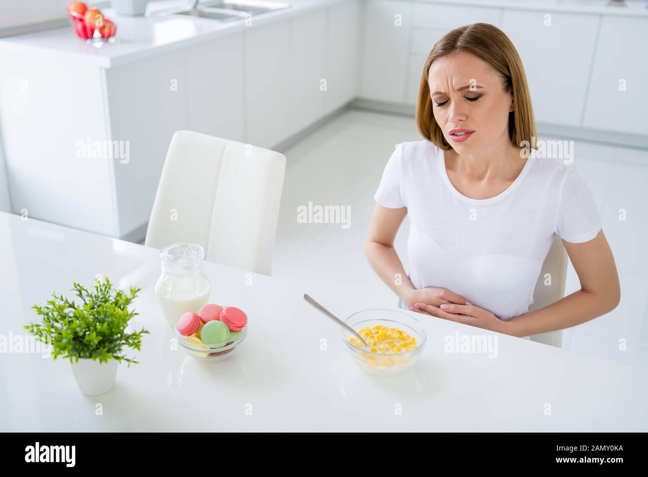 Foto ziemlich aufgebracht Hausfrau holding Bauch leiden schreckliche Schmerzen kann nicht essen Milch frühstück Cornflakes haben magenverstimmung Sitzung Tabelle weißes Licht Stockfoto