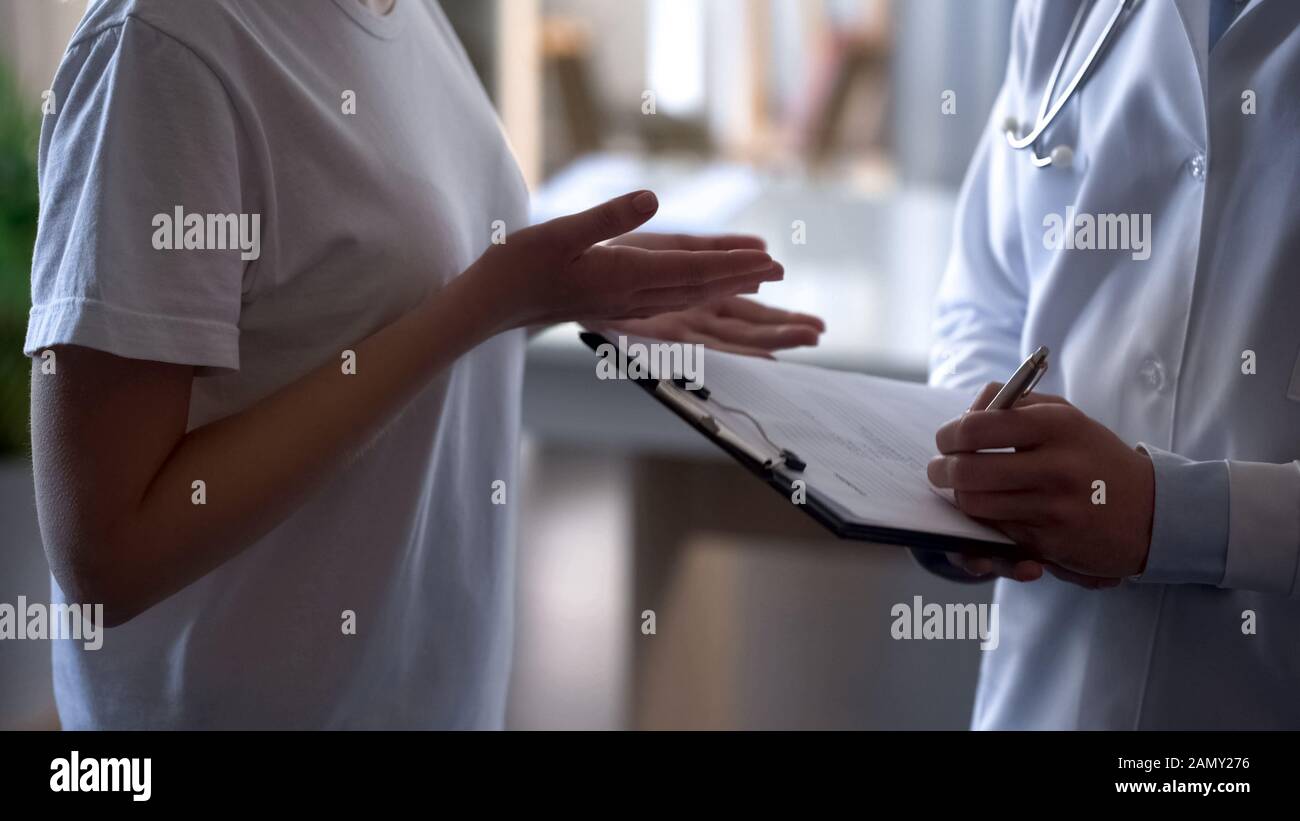 Arzt, der Patienten aufzeichnet, Beschwerden bei Kartenmädchen, die sich über gesundheitliche Probleme beschweren Stockfoto