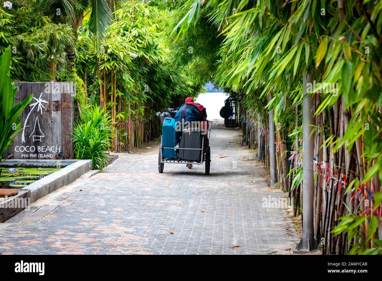 Ein Mann zieht ein Rad Warenkorb voller Touristen Gepäck von einem Resort auf Phi Phi Inseln in Thailand. Stockfoto