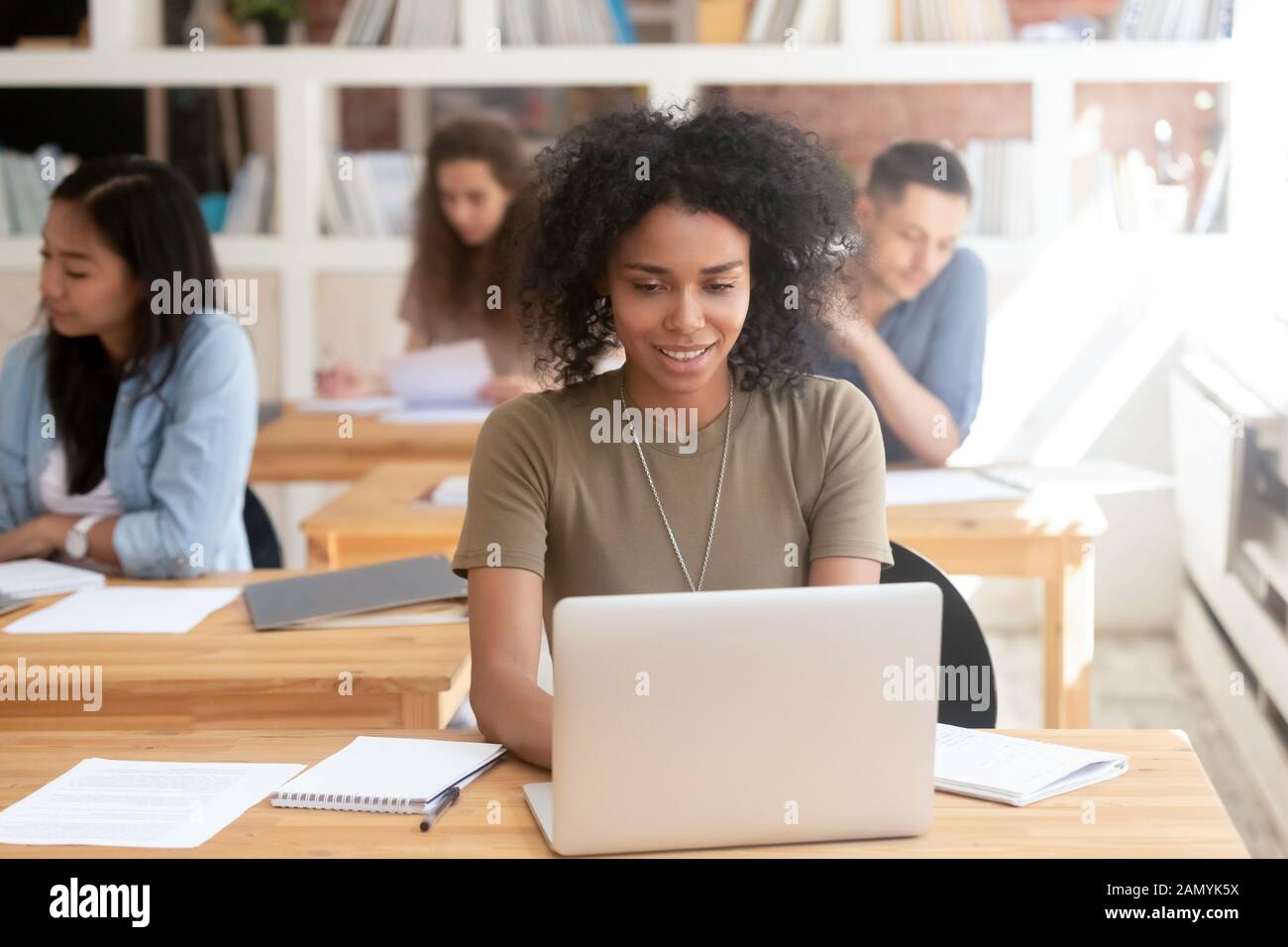 Lächelndes schwarzes Mädchen sitzt mit einem Laptop im gemeinsamen Raum Stockfoto