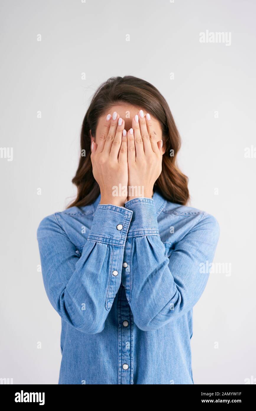 Frau, die ihr Gesicht mit den Händen bei einem Studioschuss bedeckt Stockfoto