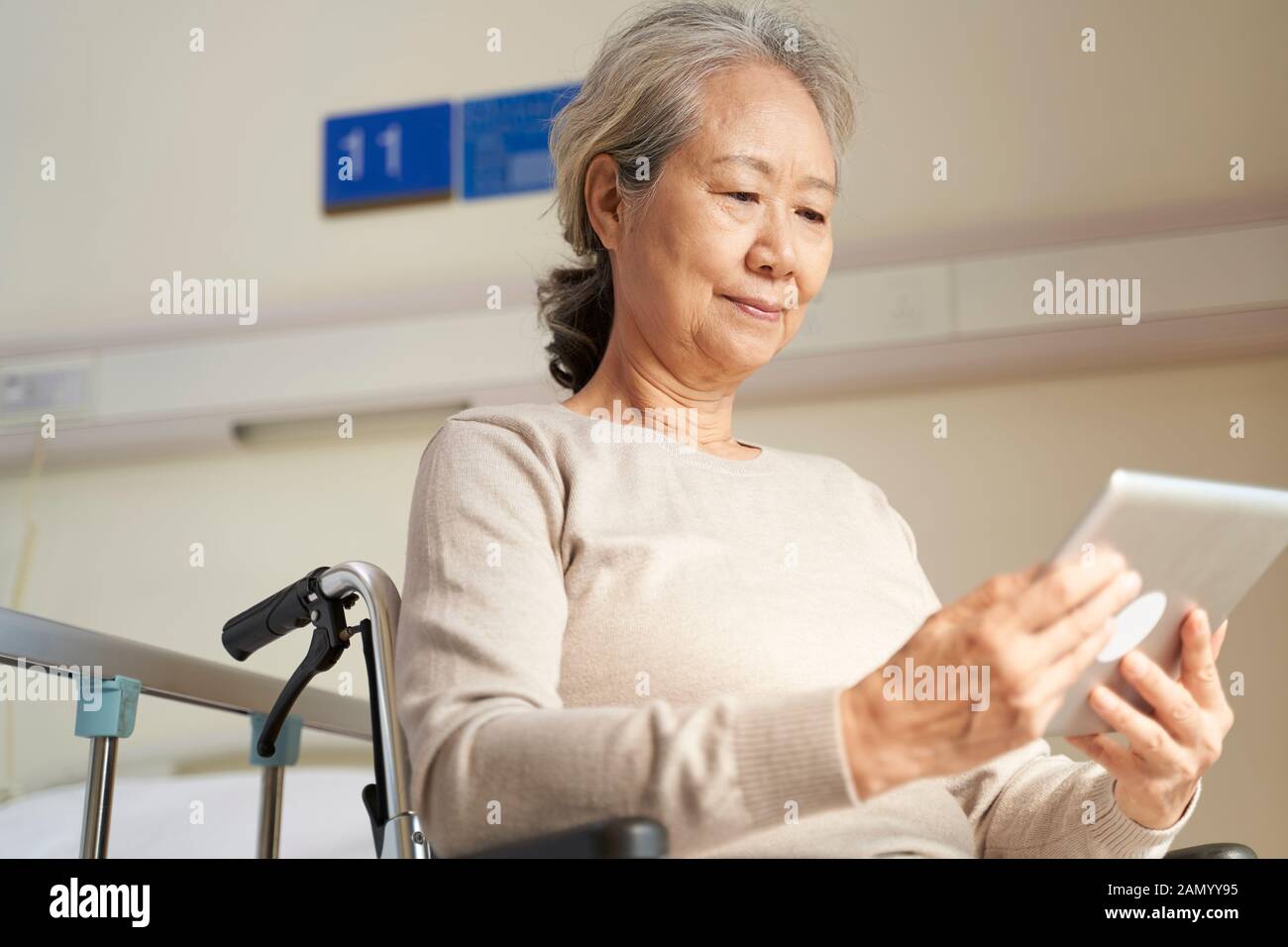 Asiatische Seniorin, die digitale Tablette in Pflegeheim oder auf der Krankenstation verwendet Stockfoto