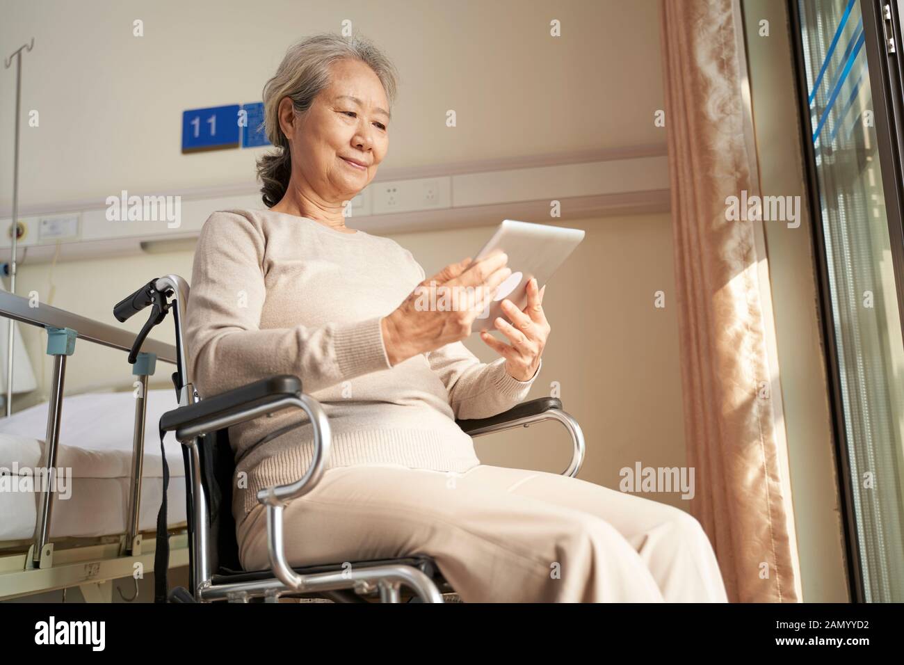 Asiatische Seniorin, die digitale Tablette in Pflegeheim oder auf der Krankenstation verwendet Stockfoto