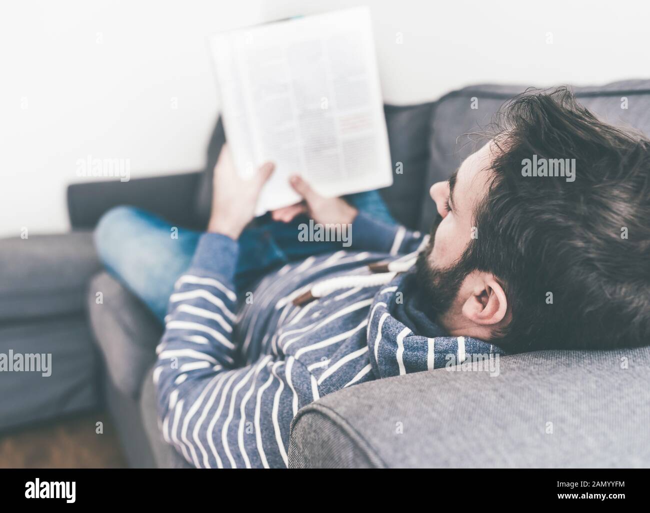 Mann, der sich auf der Couch entspannt, während er Magazin oder Zeitung liest Stockfoto