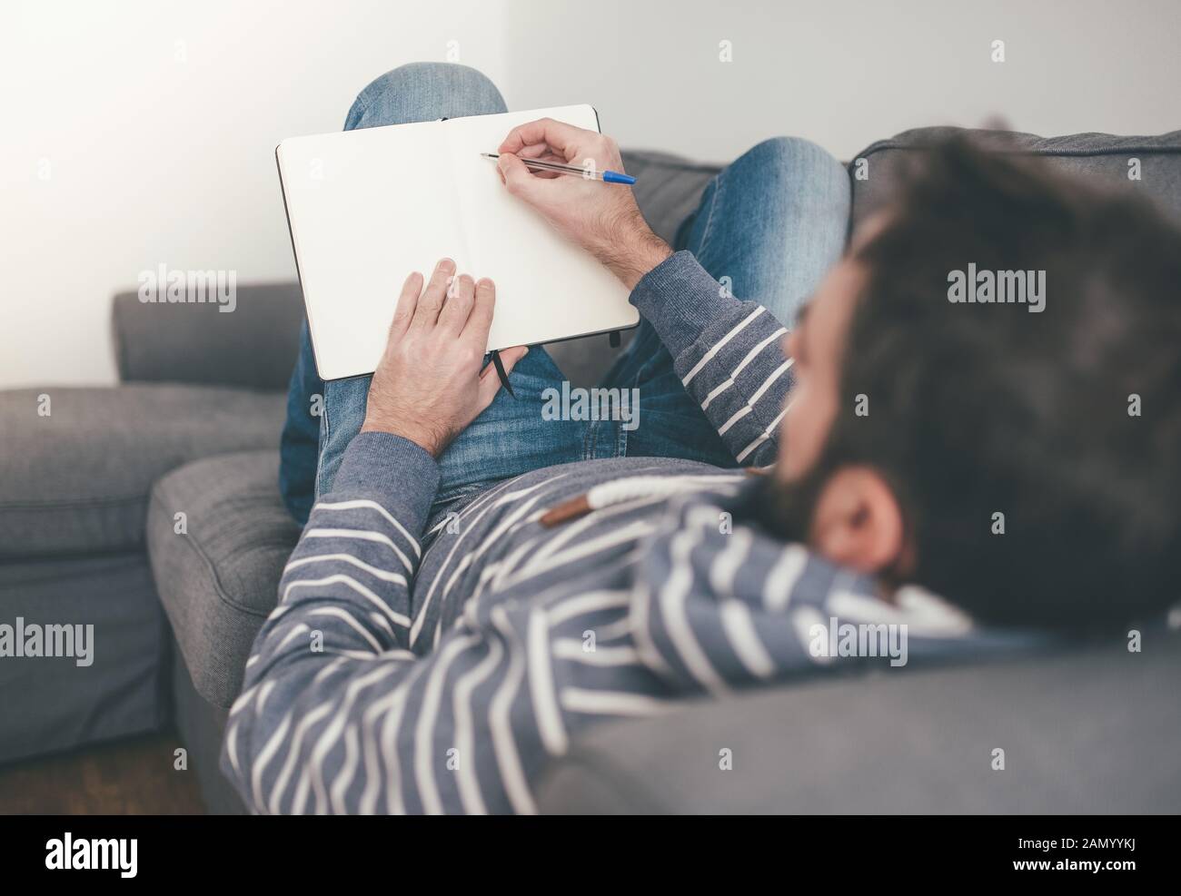Mann, der sich auf der Couch entspannt, während er Notizen nimmt oder in Tagebuch oder Notizbuch schreibt Stockfoto