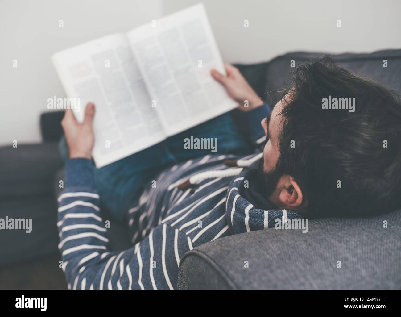 Mann, der sich auf der Couch entspannt, während er Magazin oder Zeitung liest Stockfoto