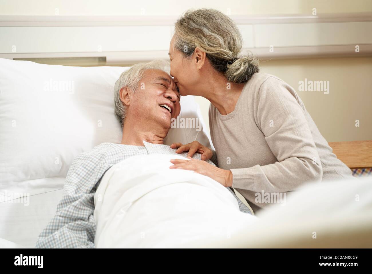 Ältere asiatische Frau küsst Ehemann auf der Stirn in der Krankenstation Stockfoto