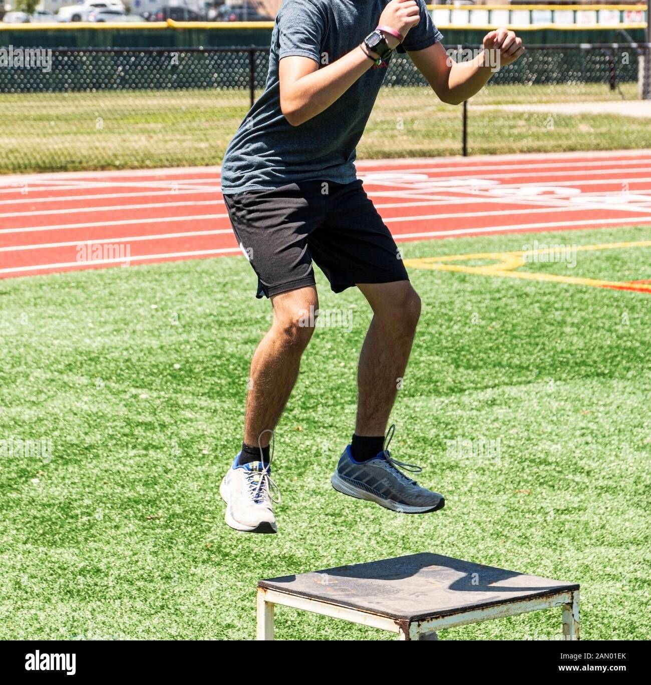 Ein High School Läufer, die Box springt außerhalb während Track Praxis auf einem grünen Rasenfeld. Stockfoto